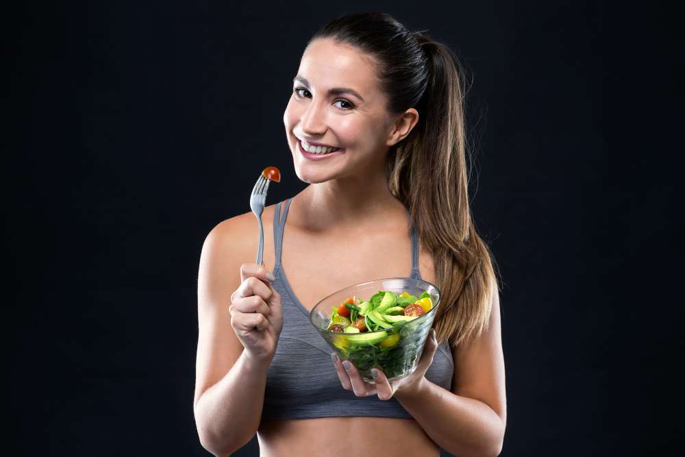 beautiful-young-woman-eating-salad-black-background